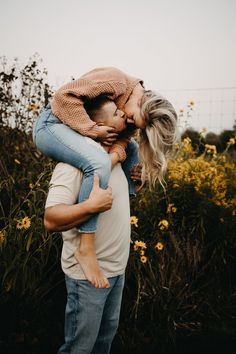 a man holding a woman on his back in front of some yellow wildflowers