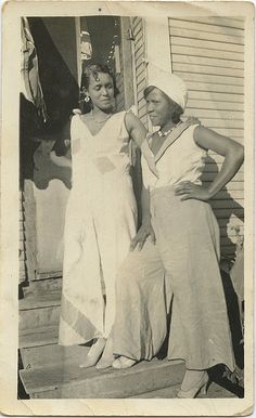 two women are standing on the steps in front of a house, one is wearing a white dress