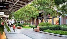 people are walking down the sidewalk in front of shops and plants on both sides of the walkway