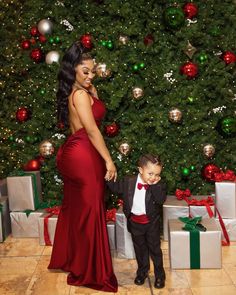 a woman in a red dress standing next to a little boy wearing a tuxedo