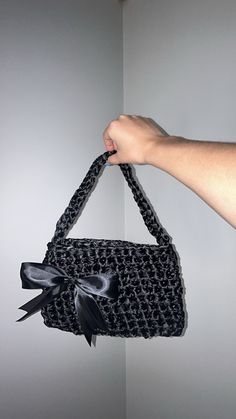 a hand holding a black purse with a bow on the front and side, hanging from a wall