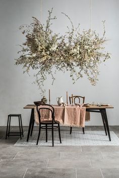 a table with chairs and flowers hanging from it's ceiling in front of a white wall