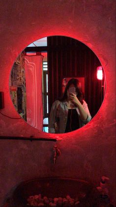 a woman taking a selfie in front of a red light mirror with her cell phone