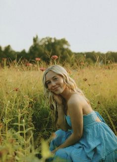 a woman in a blue dress is sitting in the middle of tall grass and flowers