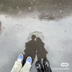 two people are standing under an umbrella in the rain, with their shadows on the ground