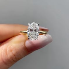 a woman's hand holding an oval diamond ring