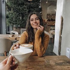 a woman sitting at a table with a cup of coffee in front of her and another person holding a spoon