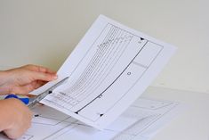 a person cutting paper with scissors on top of some drawings and blue tape around the edges