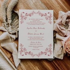 the wedding stationery is laid out on a wooden table with flowers and feathers around it