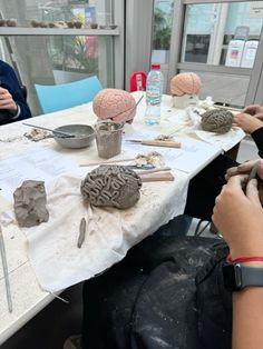 two people sitting at a table working on clay sculptures