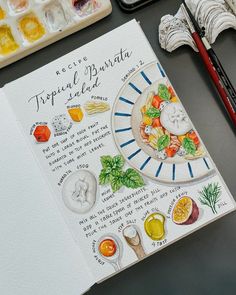 an artist's workbook with watercolors and paintbrushes on the table