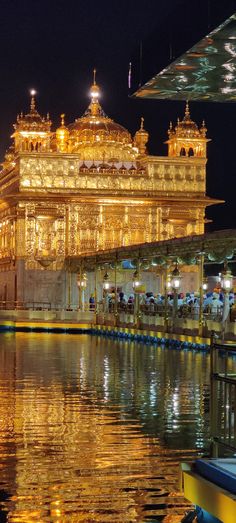 the golden building is lit up at night by boats in the water and people walking around