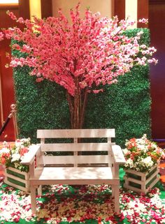 a white bench sitting in front of a tree with pink flowers on the ground next to it