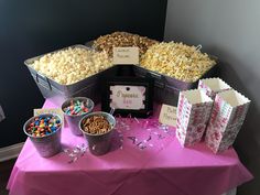 a table topped with buckets filled with lots of candy next to bags and popcorn