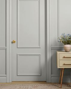 a vase with flowers on a table in front of a gray door and white paneled walls