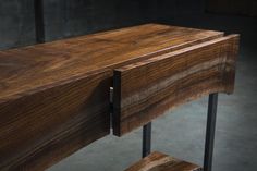 a wooden table with metal legs and a drawer on it's side, in a dark room