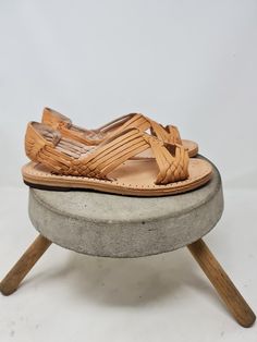 a pair of sandals sitting on top of a cement stool with wooden feet and straps