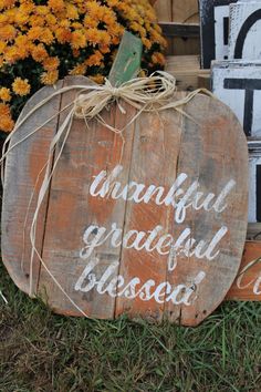 a wooden pumpkin with the words grateful grateful closed on it sitting in front of some flowers