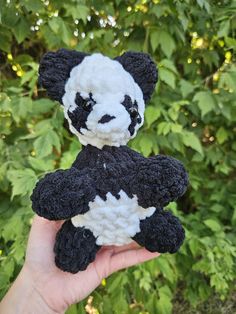 a hand holding a black and white stuffed panda bear in front of some green leaves