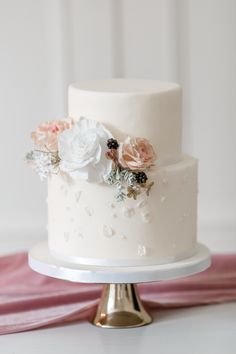 a white wedding cake with pink and white flowers on the top is sitting on a table