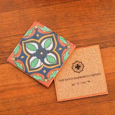 two coasters on top of a wooden table with a business card in the middle