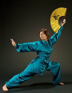 a woman in blue is holding a yellow fan and posing for the camera with her arms stretched out