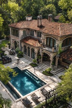 an aerial view of a large house with a pool in the foreground and trees surrounding it