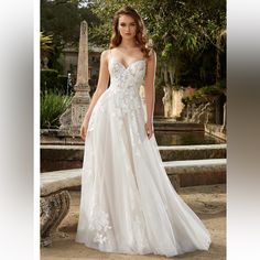 a woman in a white wedding dress standing on a stone wall with trees and fountain behind her