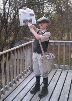 a young boy holding up a newspaper on a wooden deck with trees in the background