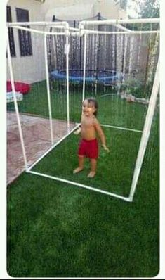 a little boy standing in front of a soccer goal on top of green grass next to a house