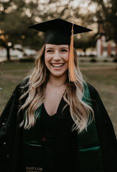 a woman wearing a graduation cap and gown smiles at the camera while standing in a field