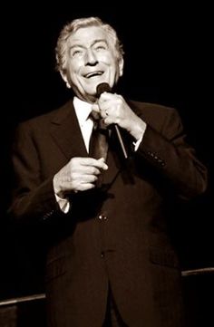 a man in a suit and tie holding a microphone up to his mouth while standing on stage