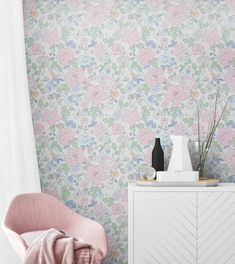 a pink chair sitting in front of a white cabinet and wall with flowers on it