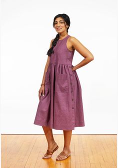 a woman standing on a wooden floor wearing a purple dress with buttons down the side