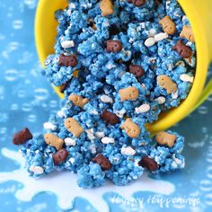 a yellow cup filled with blue and white cereal next to a pile of chocolate chip cookies