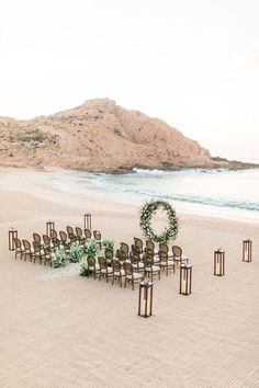 an outdoor ceremony setup on the beach with chairs and wreaths in front of it