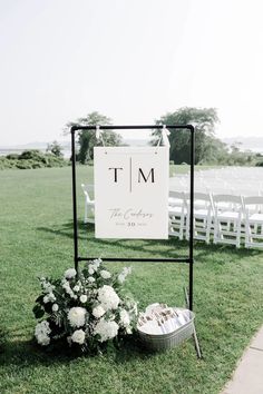 a sign that is sitting in the grass next to flowers and an empty basket with wedding rings on it