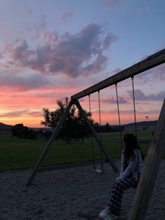 a woman sitting on top of a wooden swing set next to a lush green field