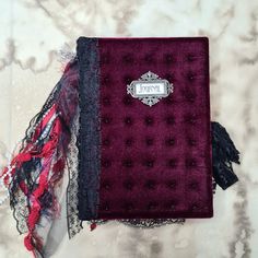 a purple book with black lace on it and a red scarf hanging from the cover