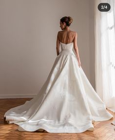 a woman in a white wedding dress is standing by a window with her back turned to the camera