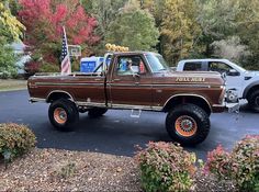 a brown truck with orange wheels parked in a parking lot next to other trucks and trees