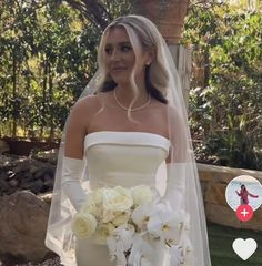 a woman in a white wedding dress holding a bouquet of flowers and wearing an arm length veil