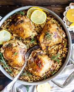 a pan filled with chicken and rice topped with lemon wedges, rosemary sprigs and sliced lemons