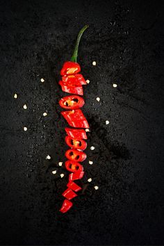 a red hot pepper on a black surface with some white seeds around it and the word food spelled out in cursive letters