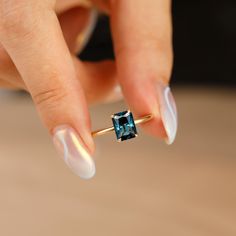 a woman's hand holding an engagement ring with a blue topazte stone