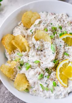 a white bowl filled with potato chips and sour cream dip surrounded by lemon wedges