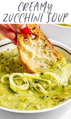 a hand dipping some bread into a bowl of creamy zucchini soup with pesto