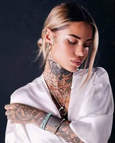 a woman with tattoos and piercings on her arm wearing a white shirt looking down