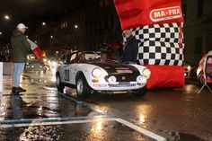 a man standing next to a race car on a wet street at night with other cars in the background