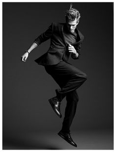 a man is jumping in the air while wearing a suit and shoes with his legs spread out